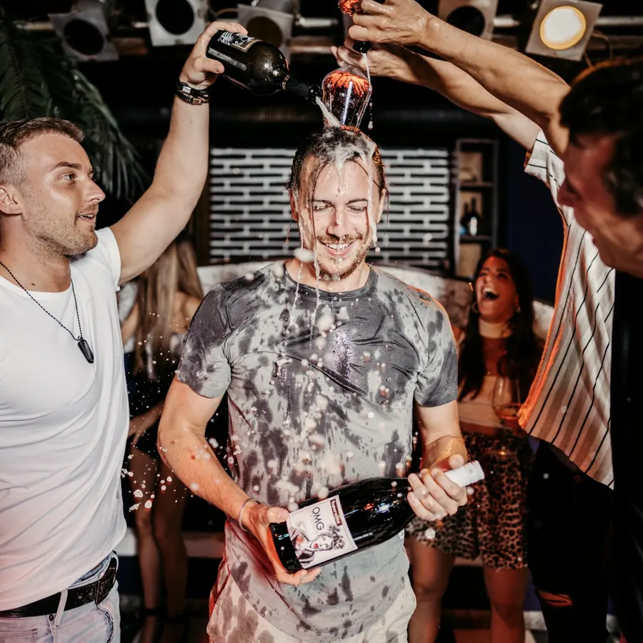 Pascal wird von Freunden mit zwei Flaschen Wein übergossen und lacht