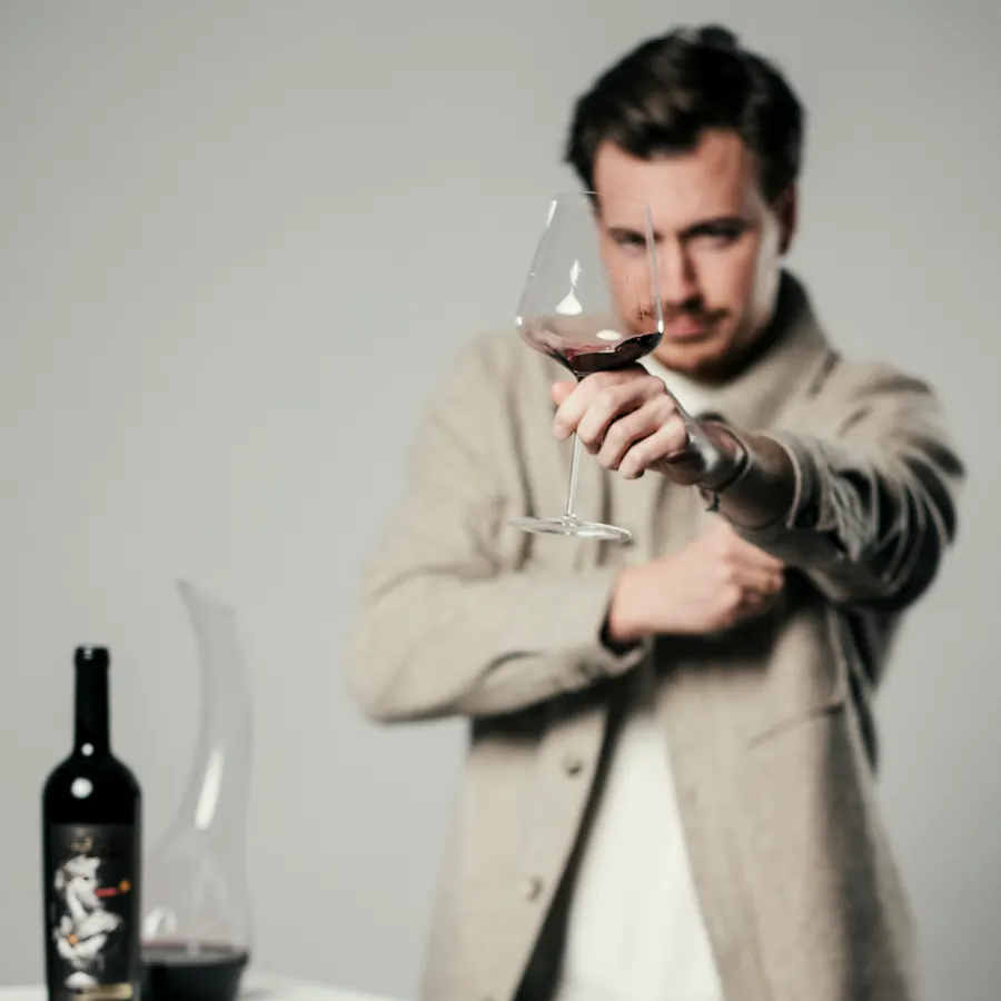 Pascal hält ein Glas Rotwein prüfend vor sich, im Studio